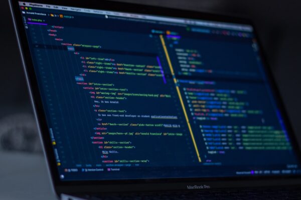 A close-up of a MacBook Pro screen displaying dark-themed HTML and PHP code in the PhpStorm editor, with syntax highlighting.