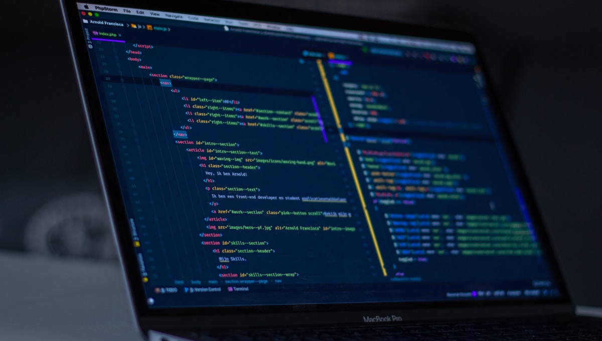 A close-up of a MacBook Pro screen displaying dark-themed HTML and PHP code in the PhpStorm editor, with syntax highlighting.